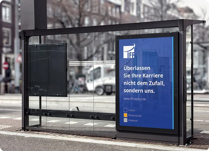 Ein Wartehäuschen zeigt eine große blaue Werbung in deutscher Sprache, die für Karriereplanung und Finanzierung wirbt. Im Hintergrund sind städtische Gebäude, Bäume und ein weißer Lastwagen durch die Glasscheiben zu sehen. IFF Akademie - kaufmännische Weiterbildung